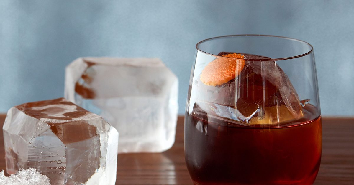 A Negroni in a rocks glass with a large clear ice cube and an expressed orange peel resting on the rim, photographed on a bar counter