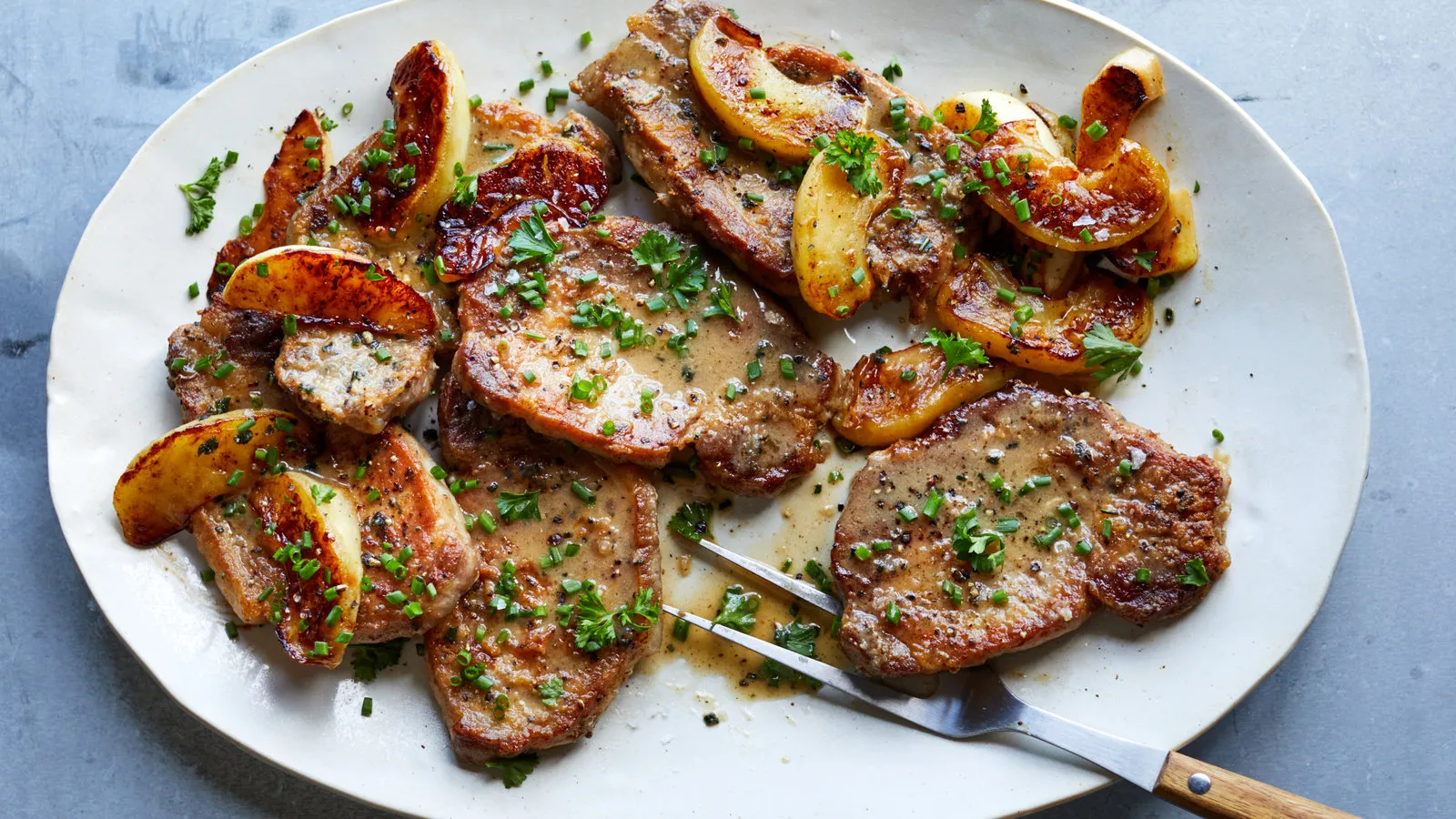 A chilled glass of hard cider beside a plated pork chop with roasted apples at a restaurant