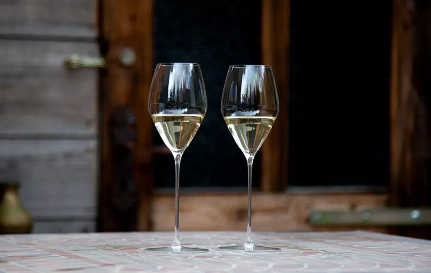 A hand holding a glass of white wine tilted over a white tabletop to show the wine color clearly