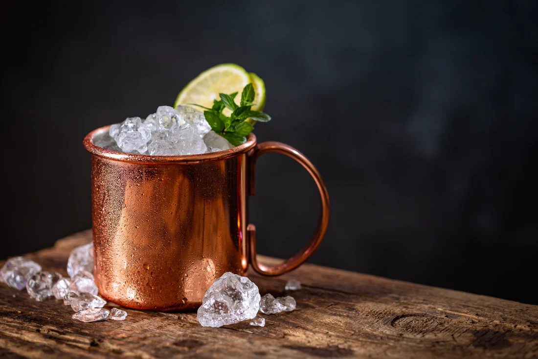 A nonalcoholic ginger-lime drink in a copper mug with mint and a lime wedge on a bar
