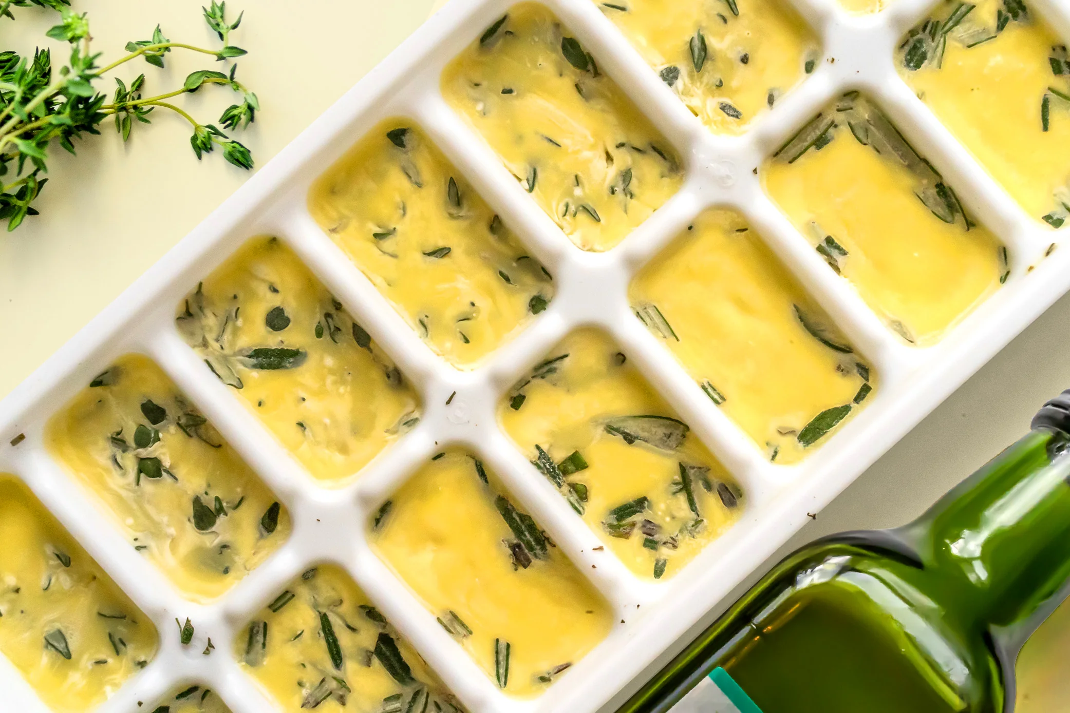 An ice cube tray filled with chopped green herbs suspended in olive oil on a kitchen counter, ready to freeze
