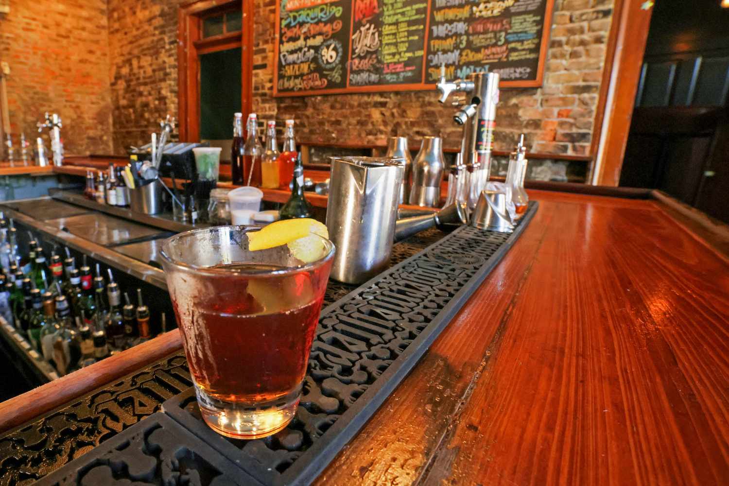 Three classic cocktails on a polished bar top: an Old Fashioned with a large ice cube, a Margarita in a coupe, and a Negroni in a rocks glass, softly lit