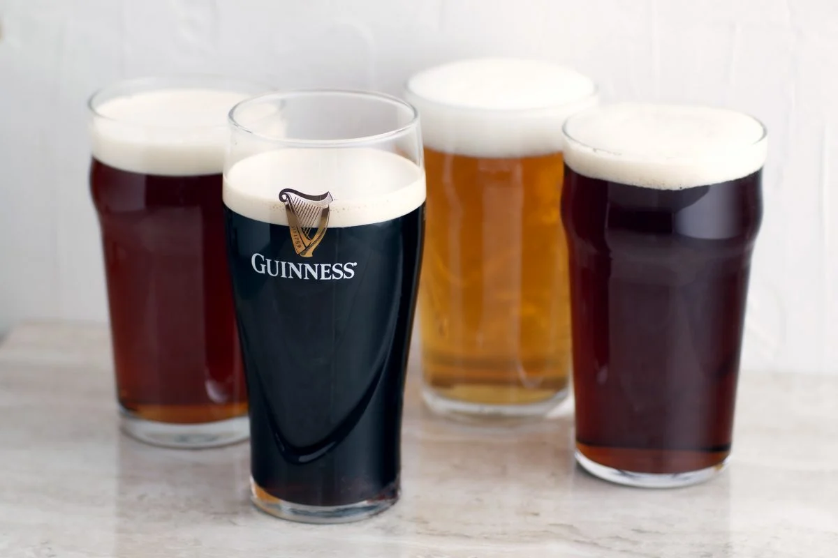 Two fresh pints on a wooden bar top, one golden lager with a foamy head and one dark stout with a creamy head, photographed in a warmly lit pub